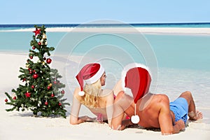 Couple Sitting On Beach With Christmas Tree And Hats