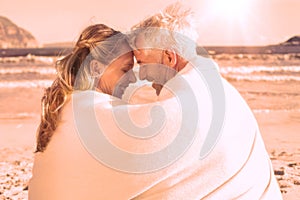 Couple sitting on the beach under blanket smiling at each other