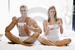 Couple sitting in bed eating cereal and smiling