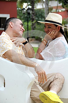 Couple sitting on a bench confidant chairs in Merida in Yucatan Mexico show their love with flirtatious looks and kisses