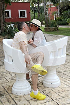 Couple sitting on a bench confidant chairs in Merida in Yucatan Mexico show their love with flirtatious looks and kisses