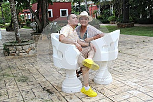 Couple sitting on a bench confidant chairs in Merida in Yucatan Mexico show their love with flirtatious looks and kisses