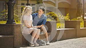 Couple sitting on bench, guy admiring blonde girl at first date, romantic mood