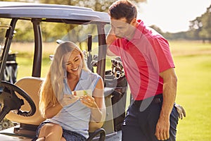 Couple Sitting In Buggy Playing Round On Golf And Checking Score Card Together