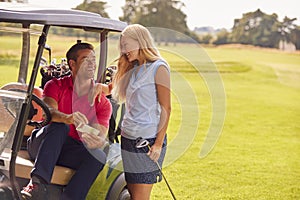 Couple Sitting In Buggy Playing Round On Golf Together