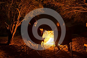 Couple sitting at burning camp fire in the night. Camping in the forest under starry sky, Namibia, Africa. Summer adventures and e