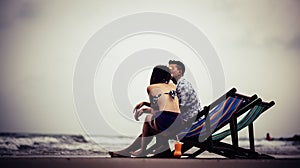 Couple Sitting On Chair At Beach Against Sky