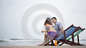 Couple Sitting On Chair At Beach Against Sky