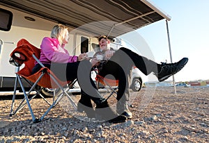 Couple sitting on chairs near motorhome drinking tea