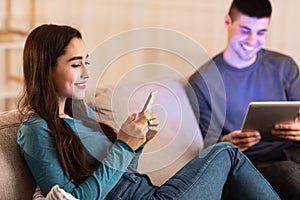 Couple sitting on couch using tablet and cell phone