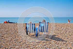 Couple sitting in deckchairs on a beach.