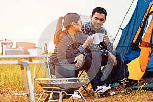 Couple sitting and drinking coffee to happily near the lake at outdoors camping. Lifestyle, holiday, long weeked and camping