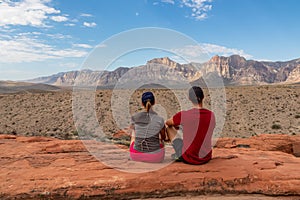 Couple sitting on edge of Calico Hills cliff with scenic view of limestone peaks Mount Wilson and Rainbow Mountain