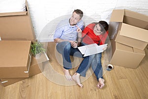 Couple sitting on floor moving in a new house or apartment flat using computer laptop