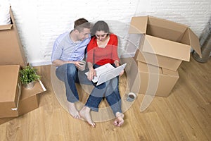 Couple sitting on floor moving in a new house or apartment flat using computer laptop