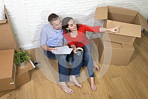 Couple sitting on floor moving in a new house or apartment flat using computer laptop