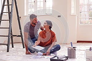 Couple Sitting On Floor With Paint Chart Ready To Decorate New Home