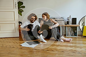 Couple sitting on floor and stroking cats while listening music on vinyl player with records