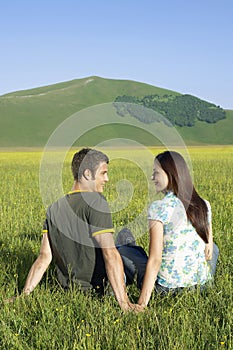 Couple Sitting On Grassy Field At Against Mountain