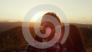 Couple sitting in grassy field at sunset. Hikers resting after hike in mountains