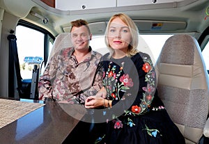 Couple sitting inside of recreational vehicle looking at camera