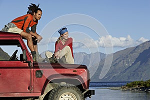 Couple Sitting On Jeep By Mountain Lake