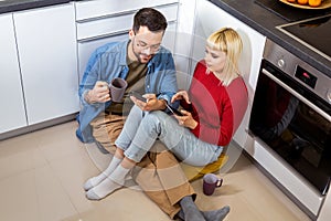 Couple sitting on the kitchen floor looking and smiling on their phones