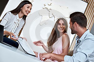 Couple sitting with manager at the travel agency office and reviewing contract