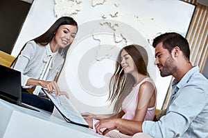 Couple sitting with manager at the travel agency office and reviewing contract