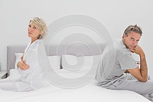 Couple sitting on opposite sides of bed looking at camera