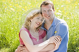 Couple sitting outdoors holding flower smiling