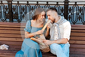 Couple sitting on the park bench and eating sandwich , having fun outdoors. Dating, lifestyle concept