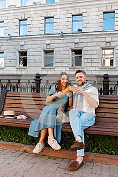 Couple sitting on the park bench and eating sandwich , having fun outdoors in sunny summer day