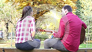 Couple sitting on park bench, man playing guitar while woman singing