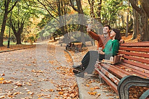 couple sitting at public park bench at autumn sunny day pointing at copy space