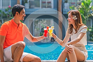 Couple sitting by resort and hotel pool together with glass of fruit juice on hand