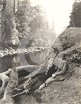 Couple sitting on rock beside stream