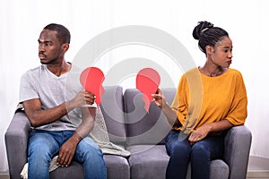 Couple Sitting On Sofa Holding Broken Heart