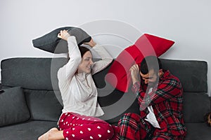 Couple sitting on the sofa at home, having fun and enjoying quality time. Couple is playing a pillow fight