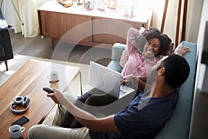 Couple Sitting On Sofa At Home Using Laptop Computer And Watching TV