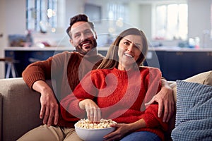 Couple Sitting On Sofa With Popcorn Watching TV Together