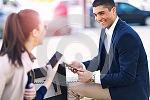 Couple sitting on solar bench and charges phone