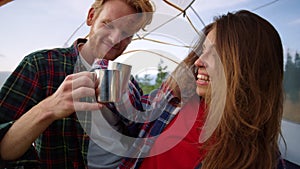Couple sitting in tent together. Happy woman and man clinking cups with tea