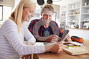 Couple sitting in their kitchen using laptop