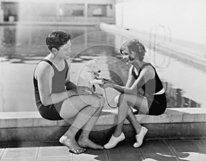 Couple sitting with their puppy next to a pool