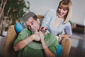 Couple sitting together on a sofa at home watching television, joyfully smiling enjoying a night in together