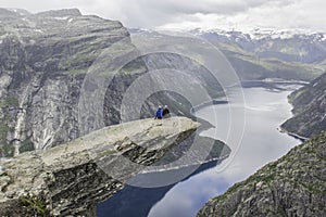 Couple sitting on trolltunga troll`s tongue rock , Norway