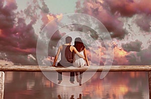 Couple sitting on wooden fence with colorful sky background