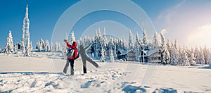 Couple in ski suits with backpack looking at beautiful view with snowy fir trees covered by snow in frozen mountains landscape.