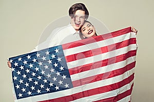 Couple on smiling faces holds flag of USA. Guy and girl happy with american flag, grey background. Travelling abroad
